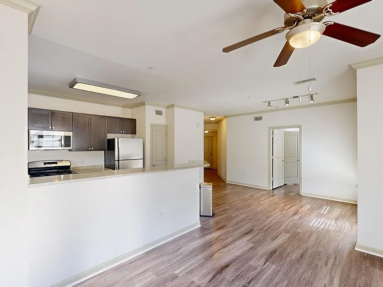 Apartment kitchen with stainless steel appliances, dining and living room with wood-style flooring.