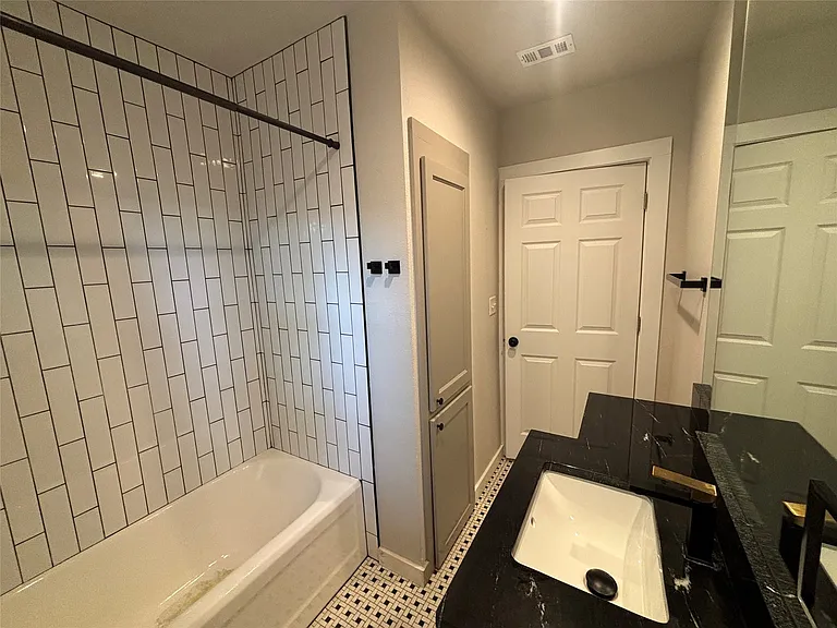 Bathroom featuring a built-in tub with white subway tile surround, black-and-white patterned floor tiling, a dark stone vanity with an undermount sink, and a built-in storage cabinet