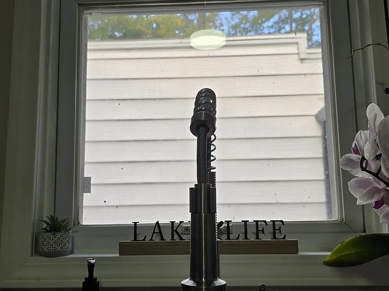 Stainless steel kitchen sink w/ extendable faucet and view of outdoors/garage.