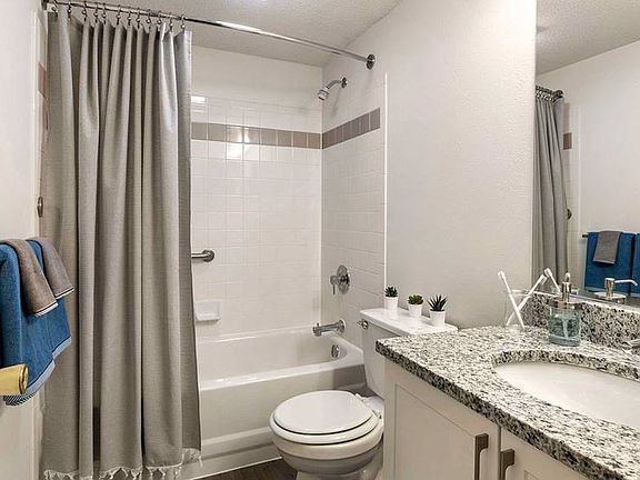 Renovated Package III bath with white cabinetry, grey granite countertops, and shower and bath with tile backsplash
