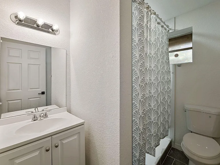 Full bathroom with a single-sink vanity, wall mirror, shower/tub combo with curtain, and a window for ventilation.