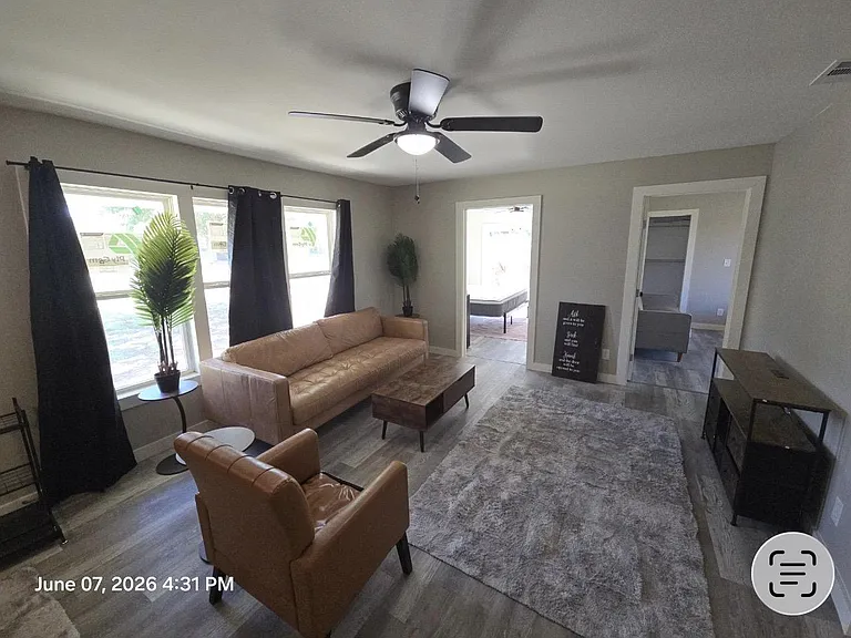 Living room with large windows, ceiling fan, and a comfortable seating area that flows into adjacent rooms.