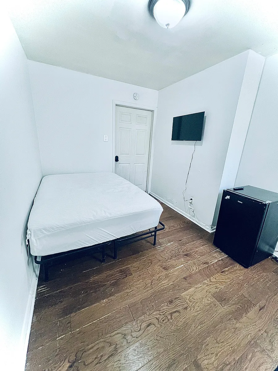 Private bedroom with hardwood floors, a wall-mounted TV, and space for a full bed plus a compact fridge. - W Somerset St