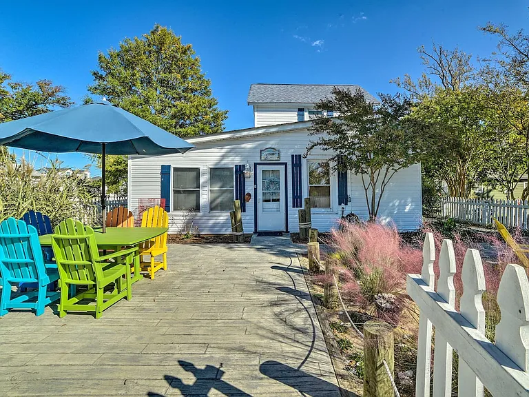 View of the front of the house and the picnic area with colorful chairs and sun umbrella.