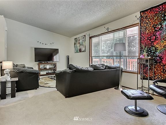 Side A living room shot from entrance. Large window on right, open to kitchen and staircase downstairs on left. 