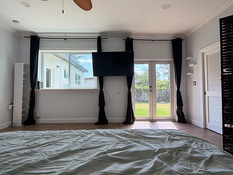 Bedroom with ceiling fan, large window and French doors to the yard, plus a closet and wall-mounted TV.