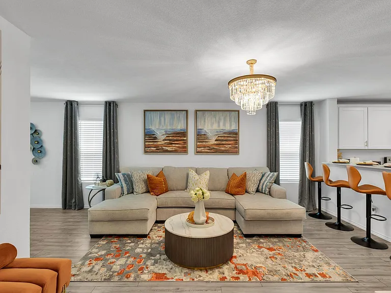Open-concept living area with sectional seating, statement chandelier, and nearby breakfast bar connecting to the kitchen.