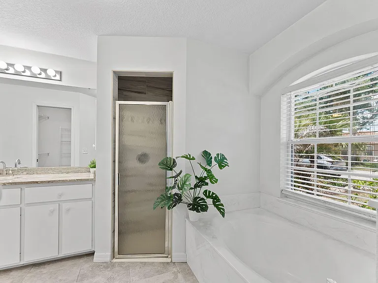 Clean bathroom with a tub/shower combo, long vanity with ample storage, and a large window with blinds.