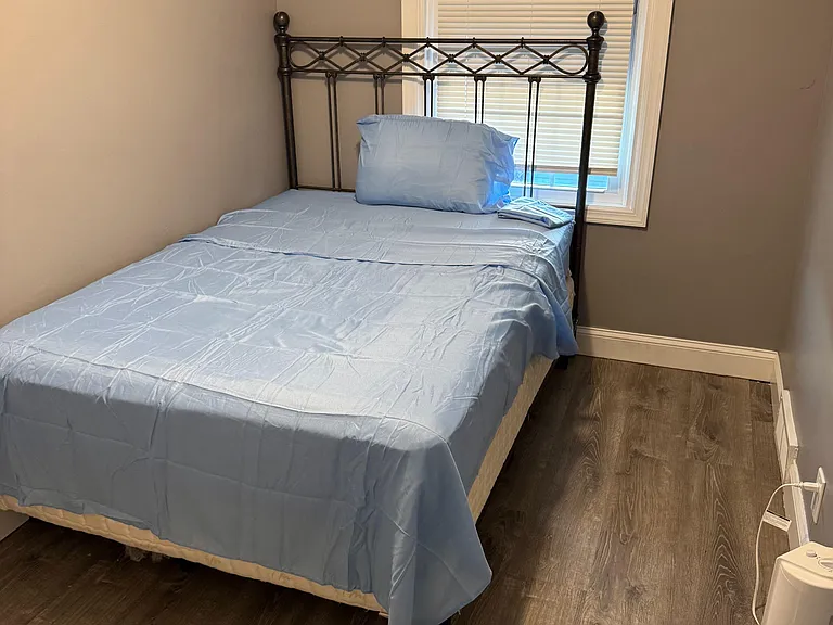 Furnished bedroom with a twin bed, durable wood-look flooring, and a window with blinds for light and privacy.