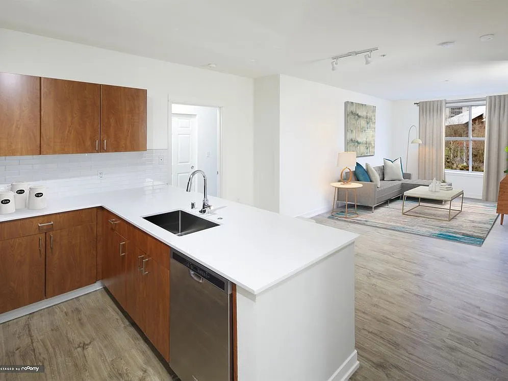 Renovated Package I kitchen and living area with white quartz countertops, oak cabinetry, stainless steel appliances, tile backsplash, and hard surface flooring - Avalon Bellevue