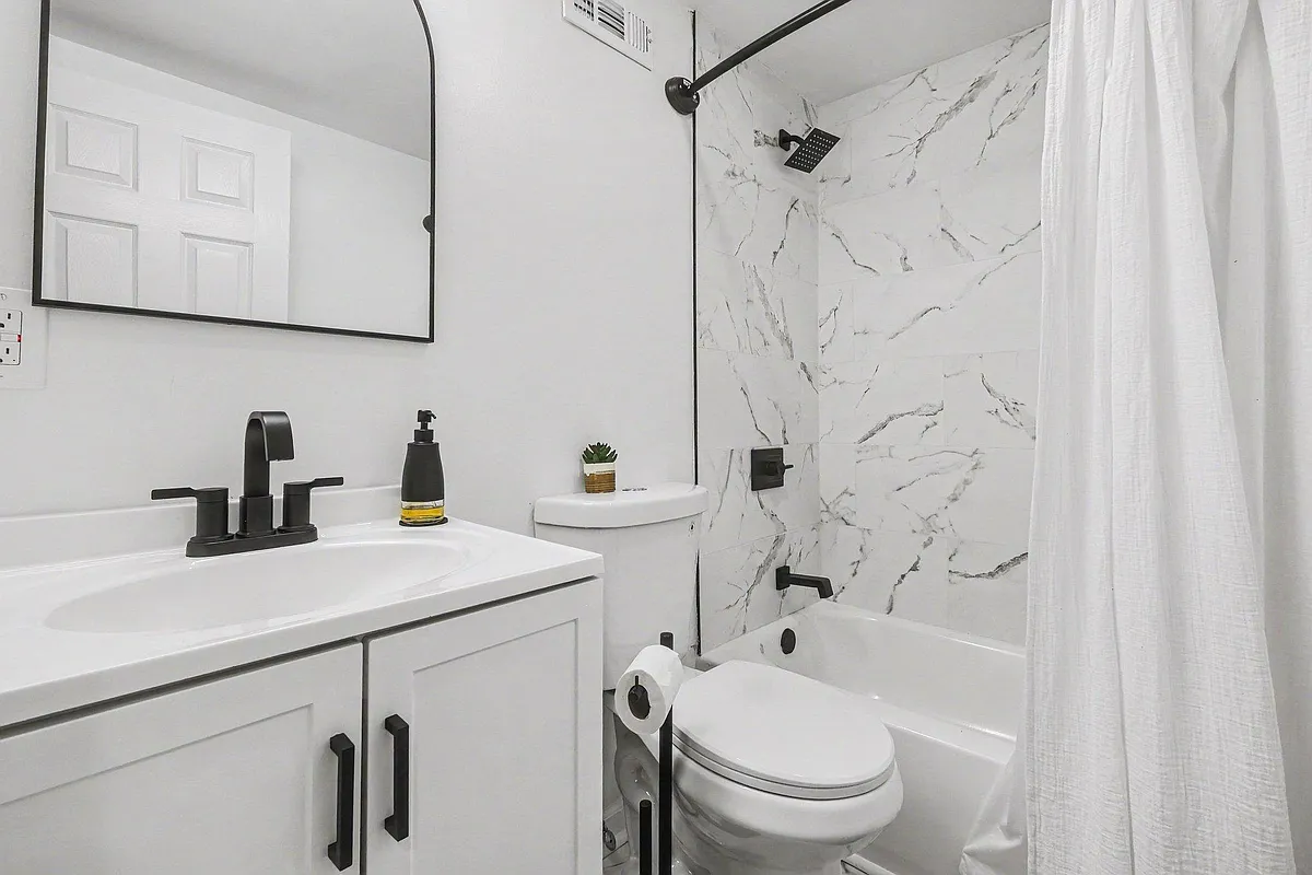 Updated full bath with tub/shower combo, marble-look tile surround, and vanity with matte-black fixtures and mirror. - Farmview Dr