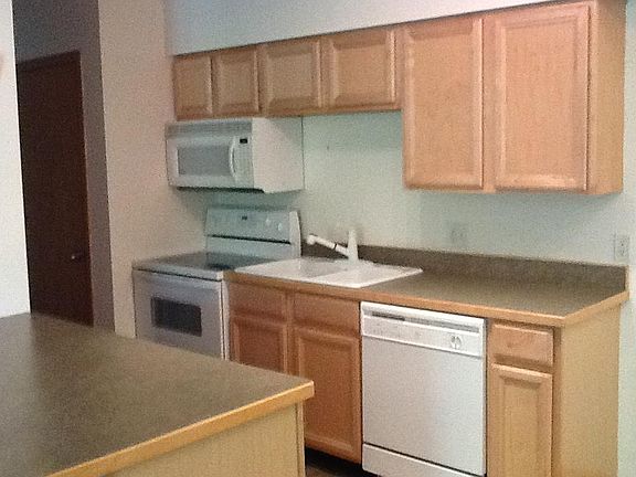 Well-equipped kitchen with glass-topped range, built-in microwave, and newer dishwasher. Breakfast bar with additional storage. Door to utility closet (with stacked washer and dryer) in the background on the right. Full-sized refrigerator and pantry on