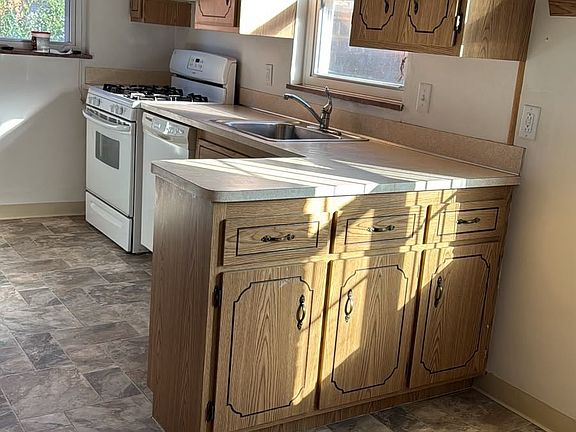 Eat-in kitchen with gas range, refrigerator, dishwasher, oak cabinetry, and new flooring.