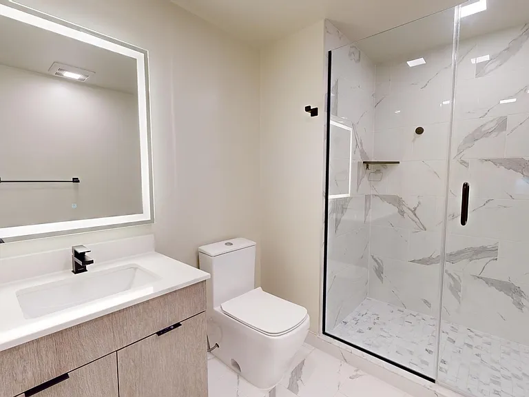 Apartment bathroom with glass-enclosed shower, tile flooring, and LED vanity mirror.