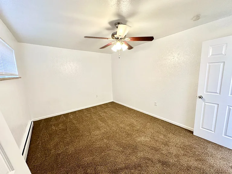 Bright, spacious bedroom featuring fresh carpet, elegant white walls, and modern ceiling fan.