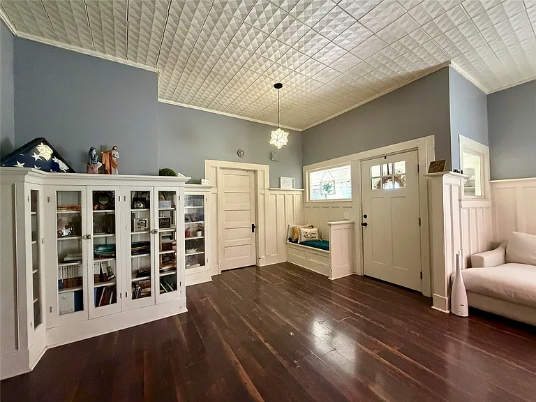 Spacious room featuring dark wood-finish flooring, a decorative pressed-tin ceiling, and white wainscoting
