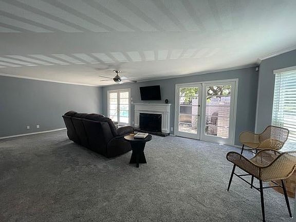 Carpeted living room featuring healthy amount of natural light, a fireplace with raised hearth, ceiling fan, and ornamental molding