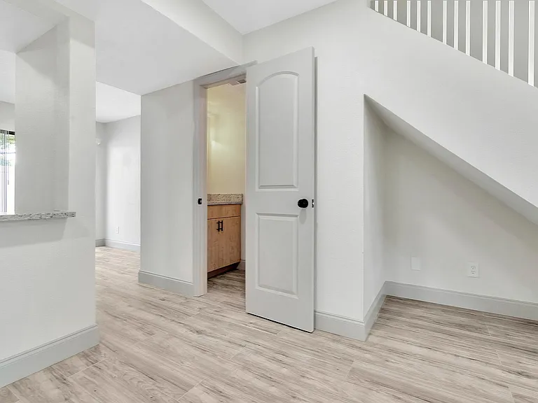 Bright and airy hallway with modern wood flooring, leading to a cozy room under the stairs.