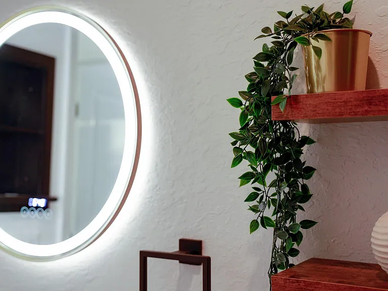 The stylish bathroom has an LED lit mirror with digital display and tasteful decorations.