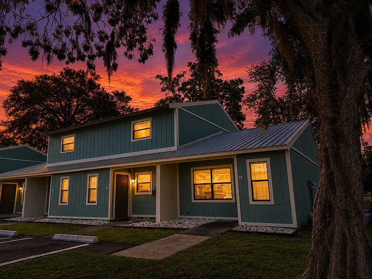 Charming duplex home at sunset with warm interior lighting and a serene sky adding to its inviting ambiance.
