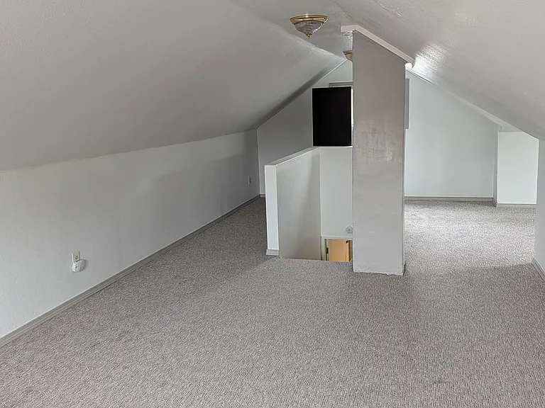 Finished loft area with carpeted flooring, sloped ceilings, and a stairwell openingideal for a flexible bonus space.