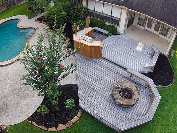 Covered porch with fan, multi-level deck, outdoor kitchen, firepit, and expansive pool decking with 