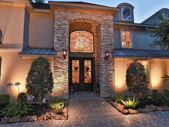 ENTER INTO ELEGANCE THROUGH DOUBLE CANTERRA DOORS WITH WROUGHT IRON ACCENTS -The stucco and stacked stone accents are highlighted by the upward landscape lighting that is stunning. The arched window above the front doors sets off the entry chandelier