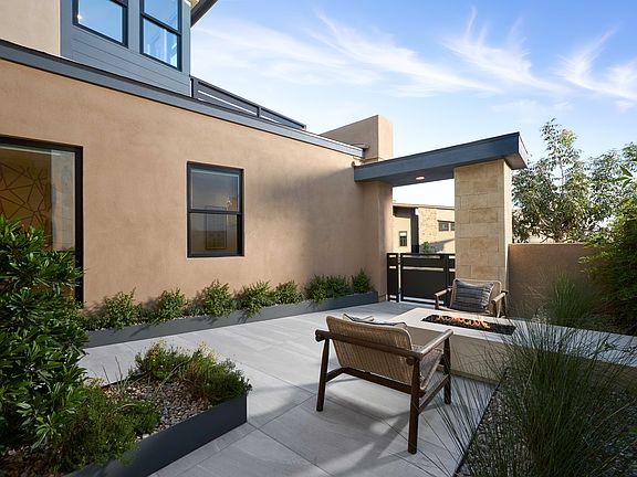 A modern, well-designed outdoor patio area with a wooden bench, surrounded by lush greenery and a cl