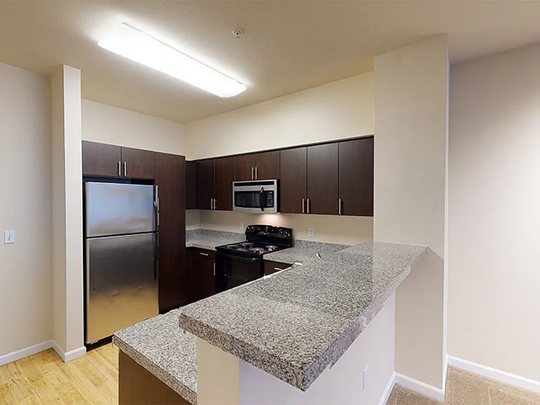 Apartment kitchen with raised granite countertops, hardwood floors, and dark wooden cabinets.