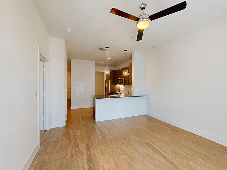 Apartment kitchen with stainless steel appliances, dining and living room with wood-style flooring.