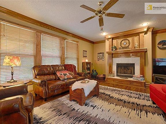 Spacious great room features a fireplace with gas logs, three large windows overlooking a stamped concrete patio and a ceiling fan.
