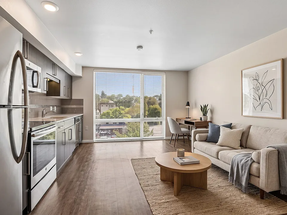 Open layout at Ludwig Apartments with a modern linear kitchen, wood-style flooring, and a large window offering natural light.