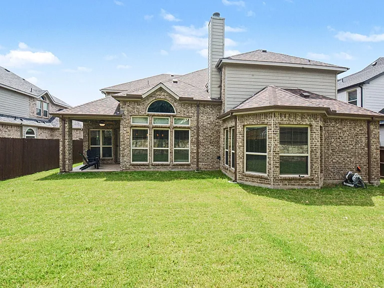 Expansive backyard featuring a manicured lawn, full brick exterior, a covered patio, a bay window extension, and a privacy fence
