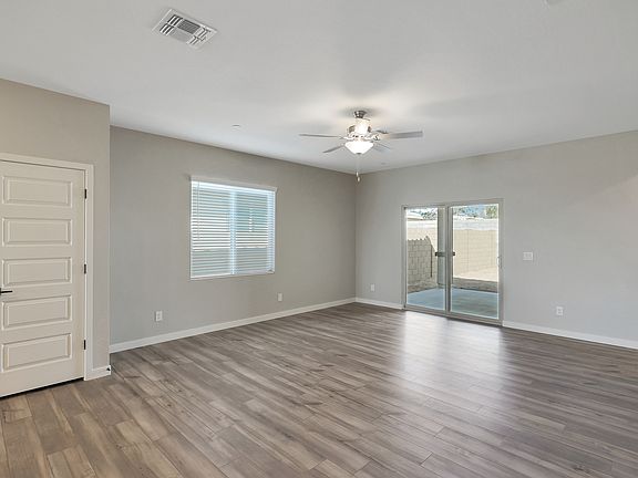 Spacious living room with wood-style flooring, a ceiling fan, and doors leading outside.