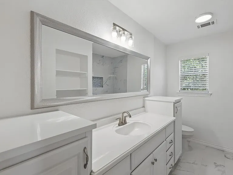 Bathroom featuring vanity, toilet, marble look tiles, a marble finish shower, and baseboards