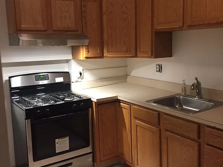 Another view of kitchen showing stove, cabinets, countertop and sink.