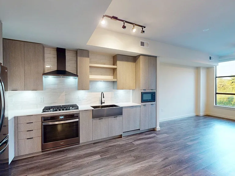 Apartment kitchen with black stainless steel appliances, dining and living room with wood-style flooring.