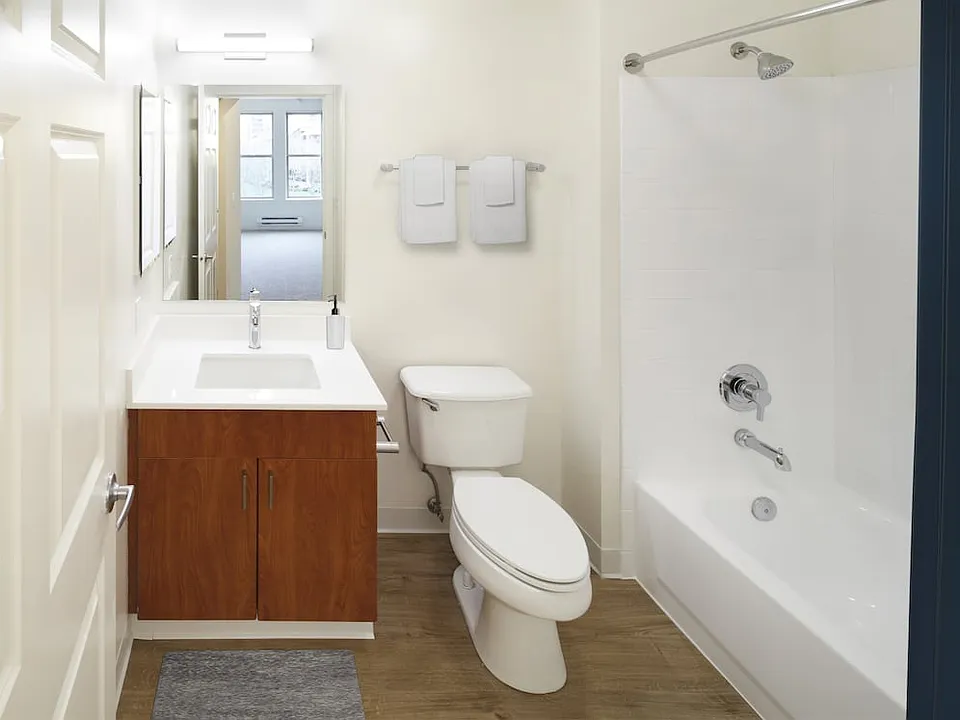 Renovated Package I bath with white quartz countertops, oak cabinetry, and hard surface flooring