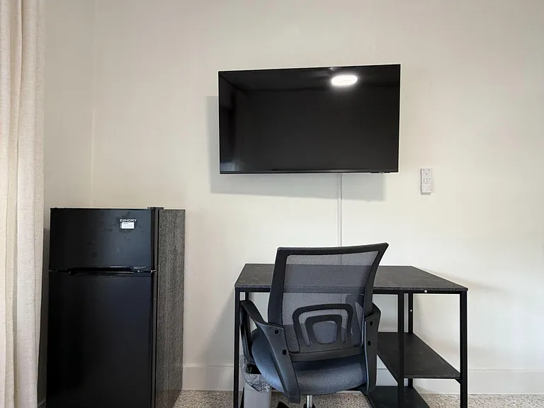 Functional in-room workspace with a desk and office chair, plus a wall-mounted TV and compact mini fridge for convenience.