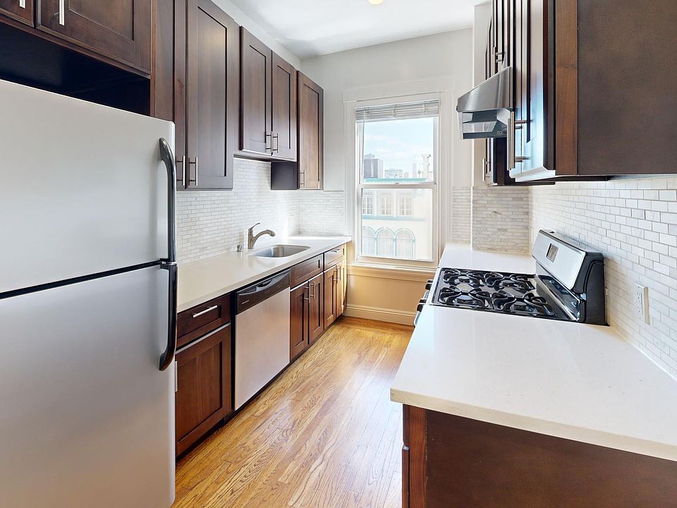 Modern kitchen with wood cabinetry, stainless steel appliances, and countertops, featuring a window with a city view.