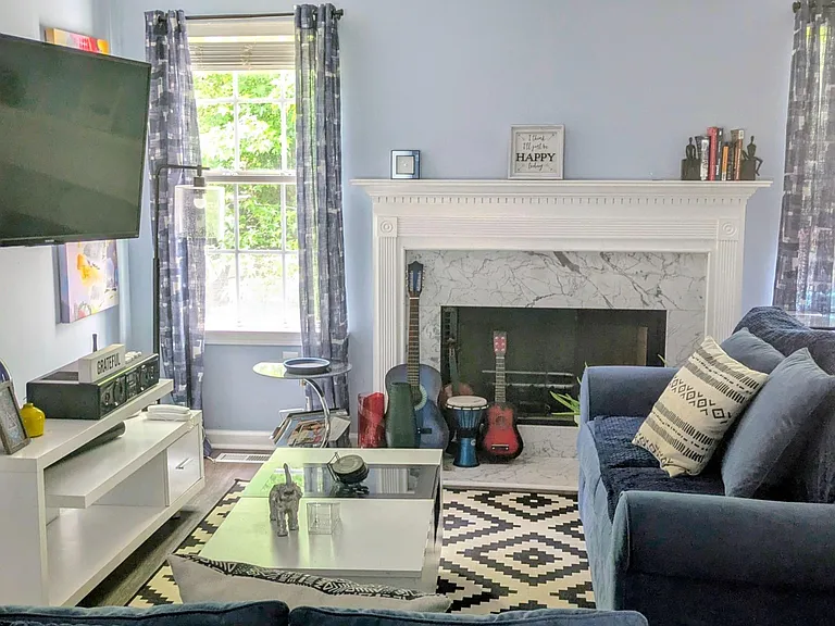 Inviting living room with a fireplace, ceiling fan, large windows, and comfortable seating for relaxing or entertaining.