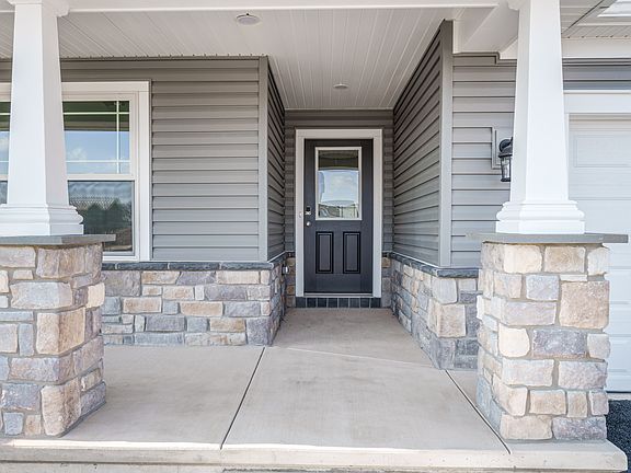 Covered front porch with stone columns, white trim, and dark entry door