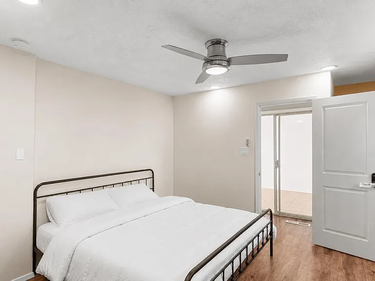 Furnished bedroom with a full bed, ceiling fan, and easy access to an adjacent tiled area through a sliding door.