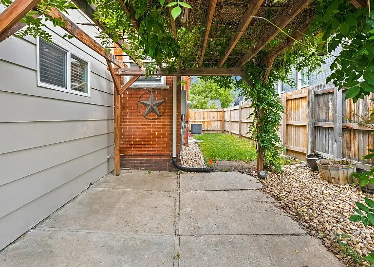 Unfurnished patio under pergola. Wisteria Vines drape purple flowers. Other side has garden boxes set up ready to go.