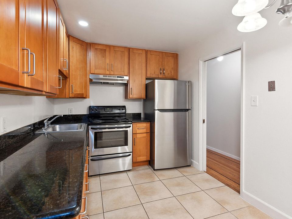 Kitchen with multiple cabinets, refrigerator, stove, range hood, and sink