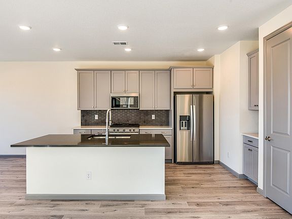 A modern, open-concept kitchen with light-colored cabinets, stainless steel appliances, and a centra