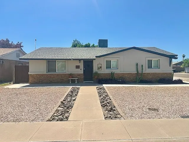 Main house exterior at La Jolla , Tempe rental home. Features a long concrete walkway flanked by stone channels, desert gravel landscaping, cactus plants, a stone veneer accent wall, and a dark front door. Welcoming curb appeal for a top Tempe, AZ stay.