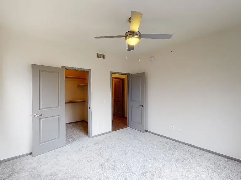 Spacious apartment bedroom with large closet and plush carpet flooring.