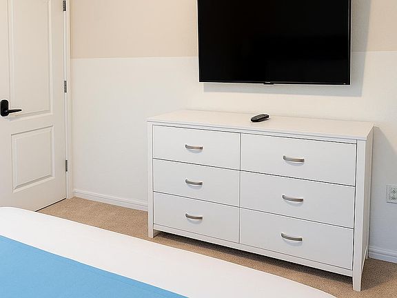 This bedroom features a wall-mounted flat-screen TV and a sleek dresser, creating a comfortable and functional space.