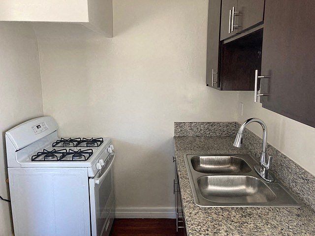 Kitchen with hardwood floors, dark wood cabinets, and gas range at The Western at Rosewood apartments in Los Angeles, California.